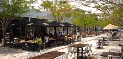 People dine in the background as sunlight pours onto a plaza with tables